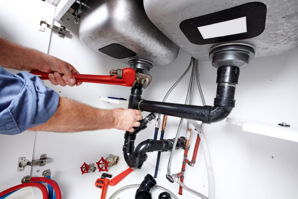Plumber repairing drain pipes beneath a kitchen sink in Gainesville